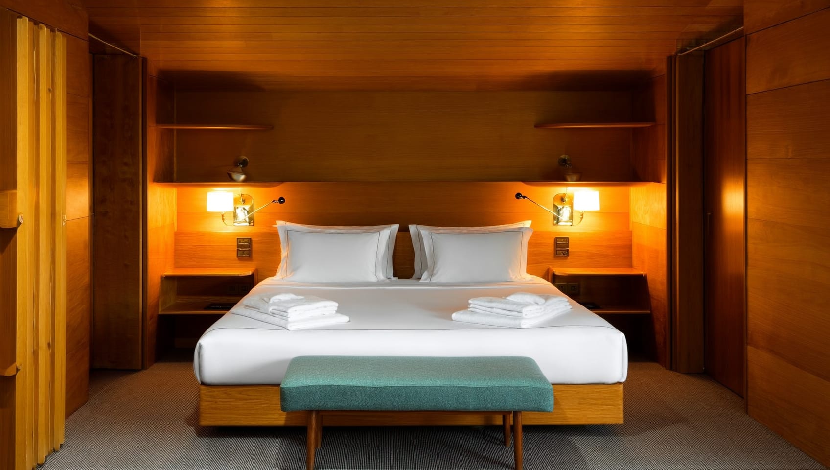 Cabin bedroom with neatly made bed and warm reading lamp