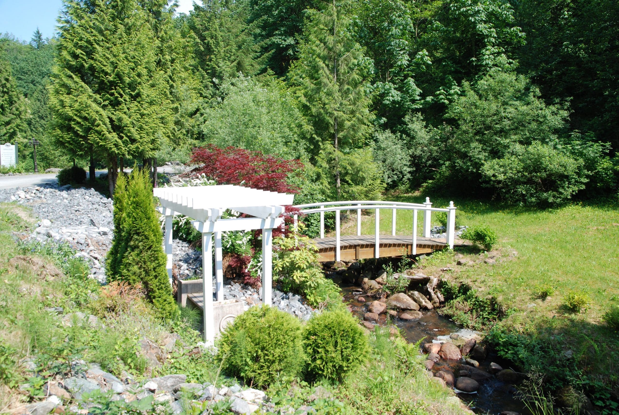 White pergola and arched footbridge over a rocky creek in the resort gardens